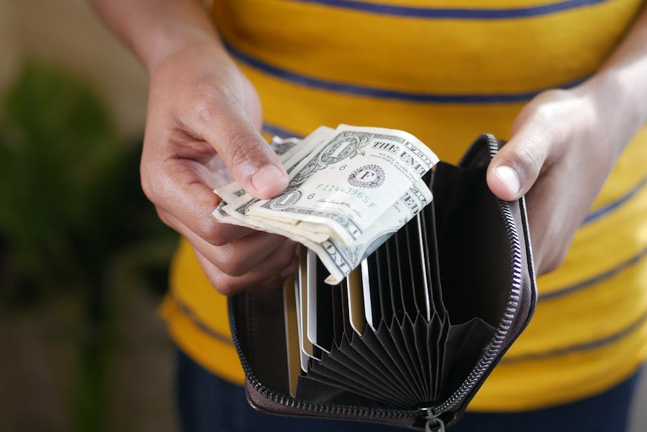 Close-up of a person s hands holding US dollar bills and a wallet.