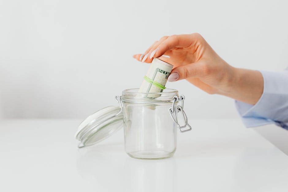 A close-up of a woman s hand putting rolled US dollar bills into a glass jar, symbolizing saving and budgeting.